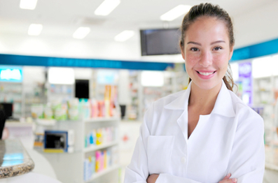 Female in a pharmacy wearing a white coat smiling with arms crossed. 